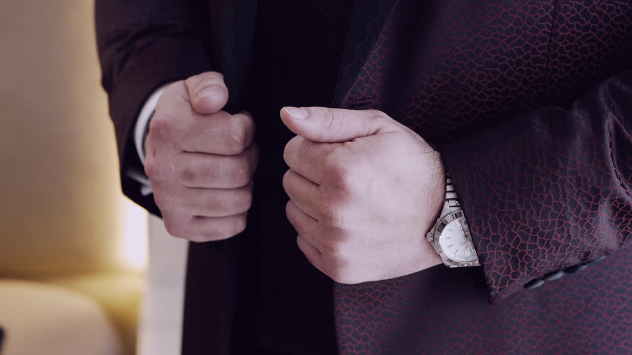 Close up of a man's hands adjusting his formal suit, wearing an elegant wristwatch