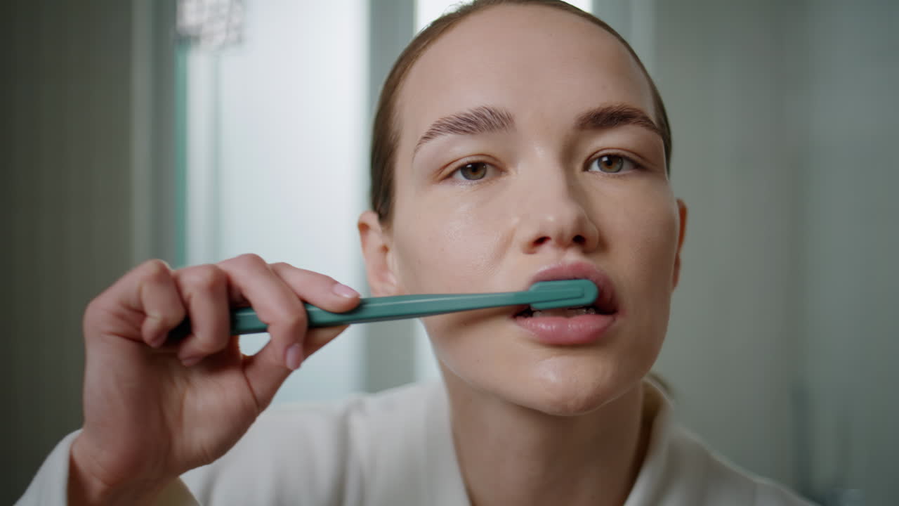 Closeup woman using toothbrush in bathroom setting. Focused girl looking camera