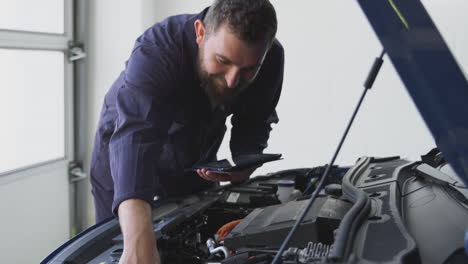 mecánico masculino en el garaje usando software de diagnóstico en una tableta digital para reparar el motor del coche