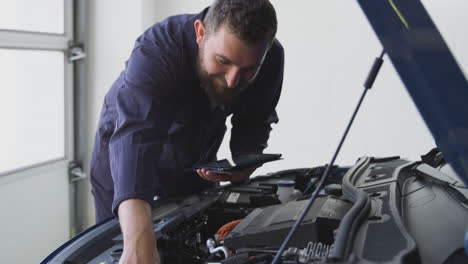 male mechanic in garage using diagnostic software on digital tablet to service car engine