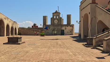 a tranquil courtyard featuring a historic clock tower under a clear blue sky, surrounded by arches and stone structures.