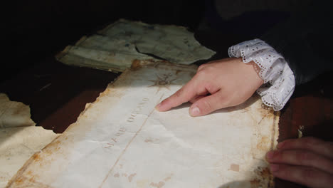 amazing slow motion cinematic shot of the finger of a person dressed in medieval clothing inside a ship's structure pointing out places on an ancient map of america