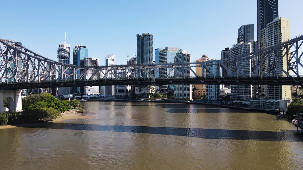 Slow pass under the heritage-listed steel cantilever Story Bridge revealing the towering urban skyline of the Brisbane City District. Aerial view