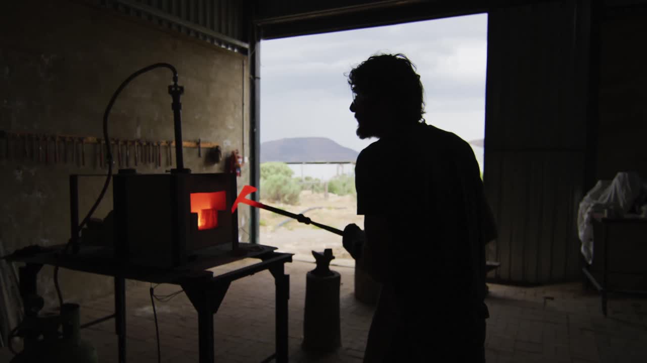 Caucasian male blacksmith holding hot metal tool in kiln with tongs in workshop