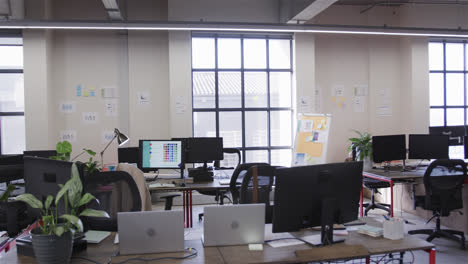 Office-workspace-with-large-windows,-chairs-and-desks-with-computers,-lamps-and-plants,-slow-motion