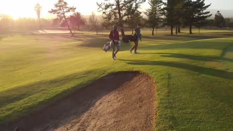 Two-diverse-male-golf-players-walking-at-golf-course-on-sunny-day