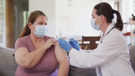 caucasian woman and female doctor wearing face masks, vaccinating