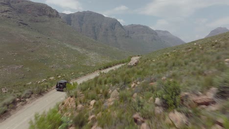 un dron vuela rápidamente sobre una carretera en un paisaje rocoso en el área silvestre de cederberg, sudáfrica, y sigue a un vehículo todoterreno que conduce en una carretera.