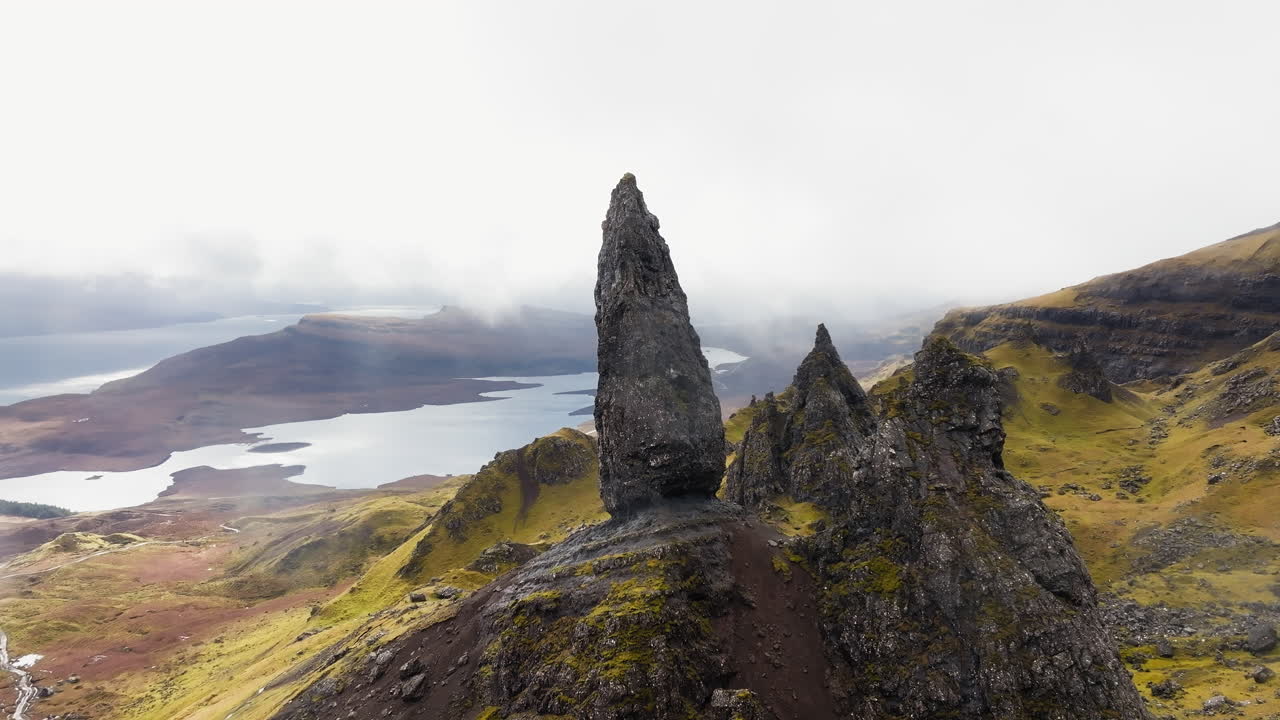 Rozsáhlý záběr dronu kroužícího kolem Old Man of Storr ve Skotsku, kde mraky a mlha činí krajinu monochromatickou a strašidelně krásnou, s dramatickými přírodními světelnými podmínkami po celou dobu.