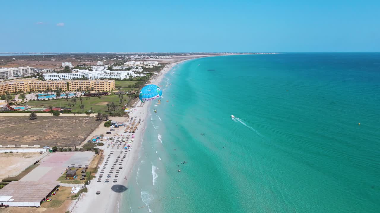 Aerial View of a Bustling Beach Resort with Parasailing and Clear Turquoise Waters