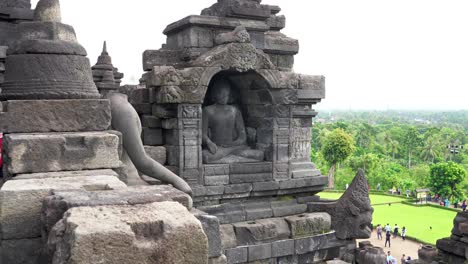 indonesia, jawa island,yogyakarta, unesco world heritage borobudur temple, beautiful buddha sculpture sitting inside the temple, outside is the greenery and the people walking around from a distance.