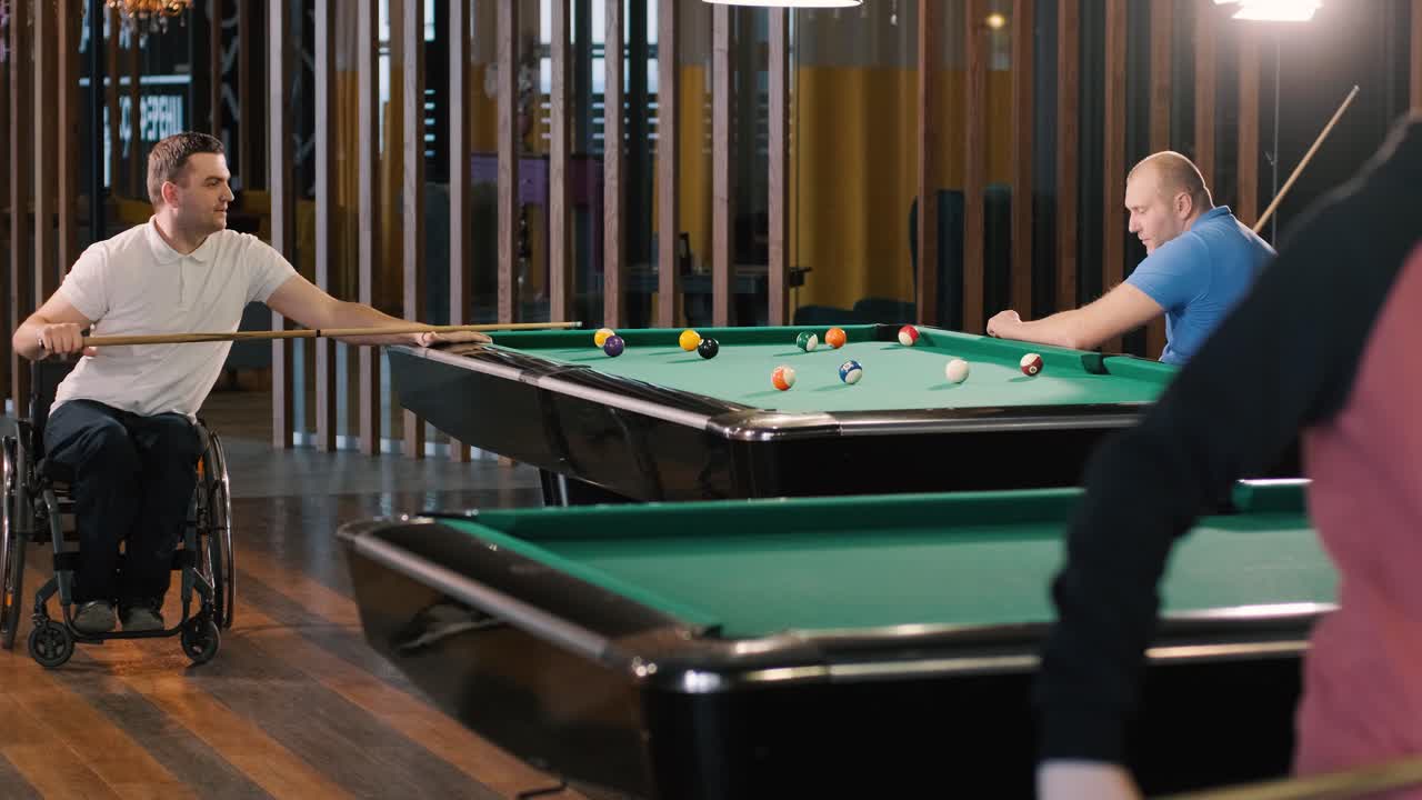 Adult men with disabilities in a wheelchair play billiards in the club