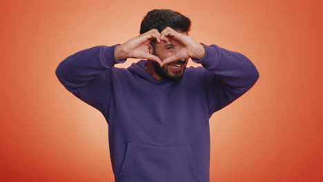 a handsome young man makes a heart shape with his hands and smiles