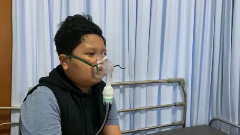 asian overweight boy makes inhalation with nebulizer in hospital