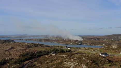 wide aerial tracking shot over sky road coast, overlooking farmland where smoke drifts in the distance. connemara landscape