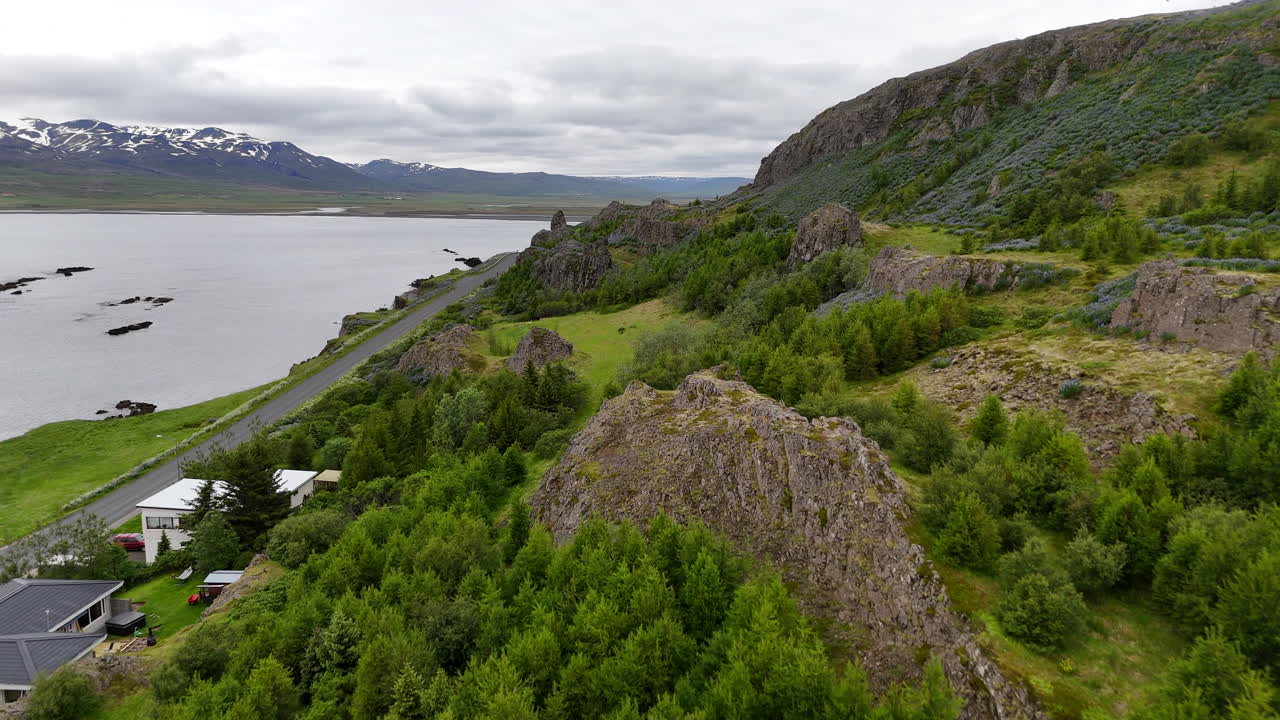 Aerial drone view of Vopnafjörður in Austurland, showing a dramatic coastline, dark cloudy skies, wide open fields, and the calm shoreline of this remote Icelandic region