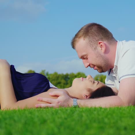 young husband with his pregnant wife relaxing in the park together lie on the green grass 2