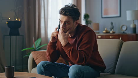 unhappy man worried call sitting couch close up. upset guy talking mobile phone