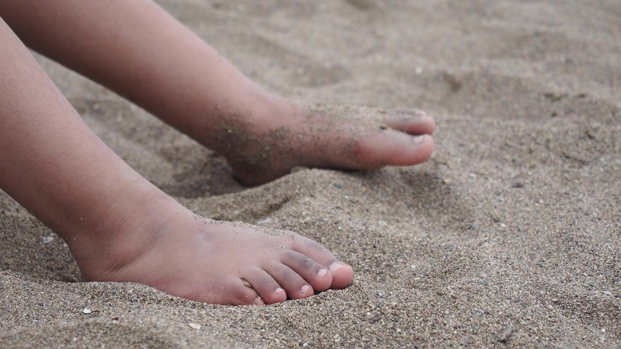 Närbild av ett barns fötter som vilar på en sandstrand
