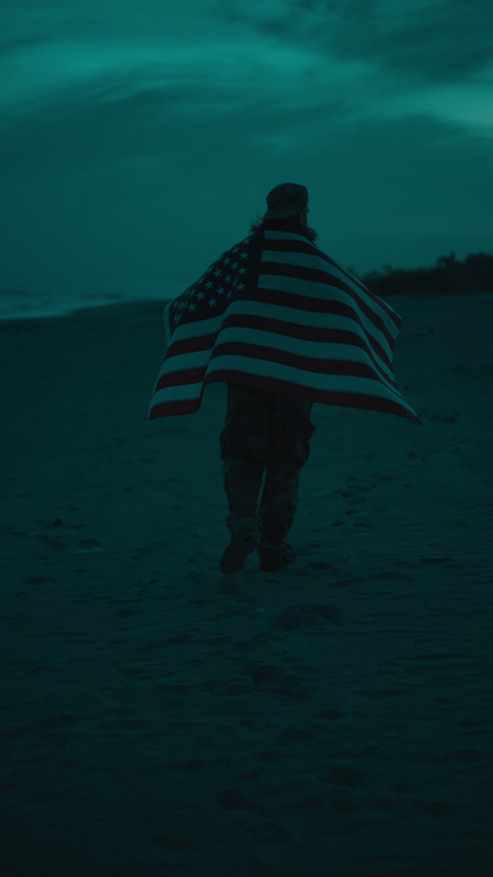 Soldato cammina sulla spiaggia di notte con la bandiera americana che sventola per il Memorial Day