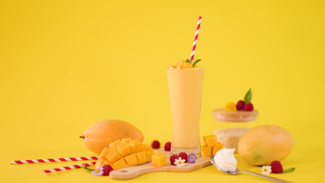 Una mano umana decora un alto frullato al mango con guarnizione di frutti di bosco su uno sfondo giallo brillante da studio