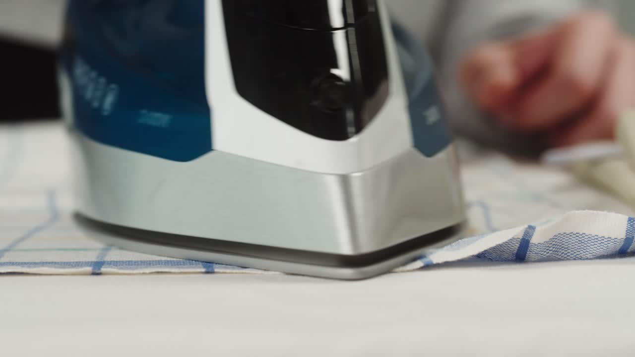 Close Up of Iron Pressing a Checkered Cloth on Ironing Board