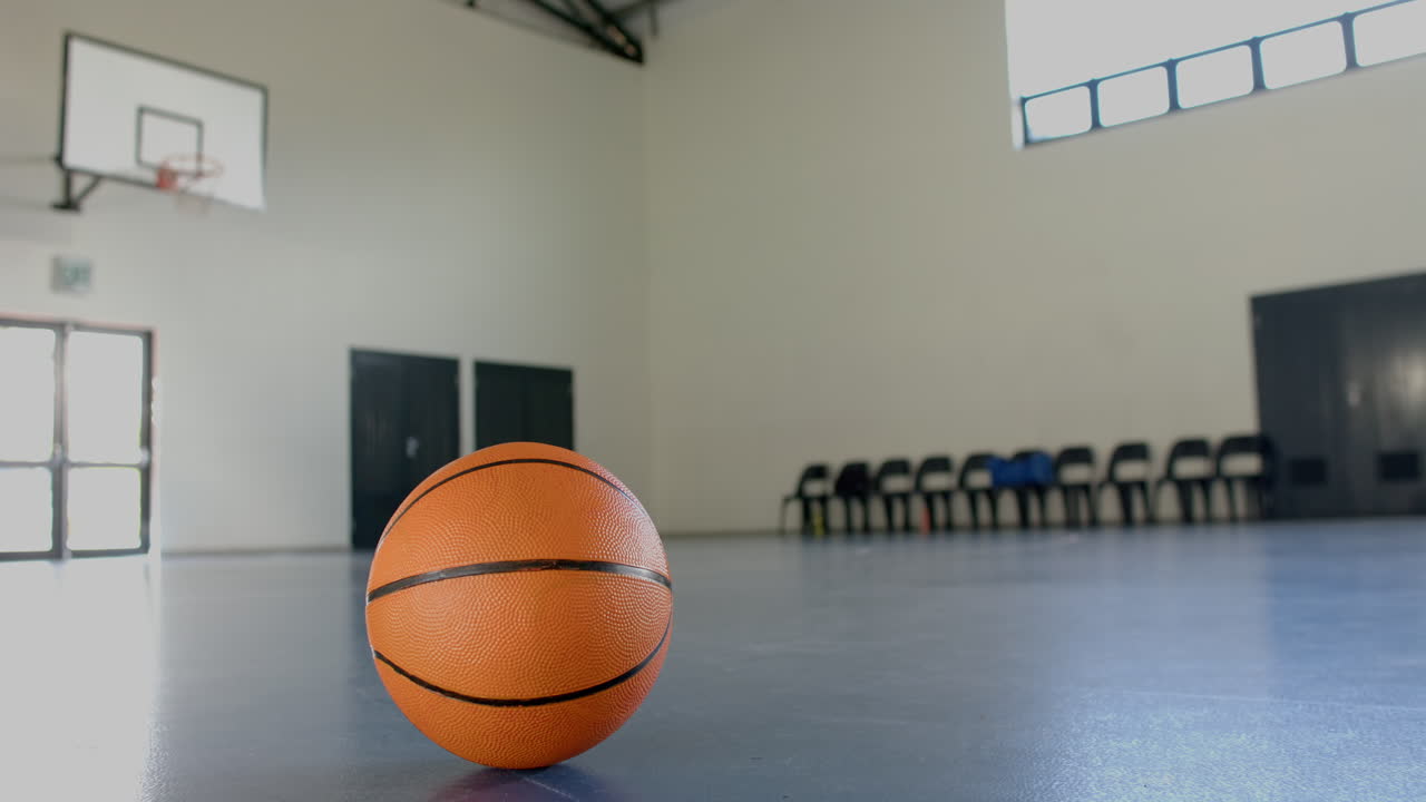 Bola basket di lantai gym di gimnasium sekolah yang kosong dengan kursi di latar belakang, dengan ruang kosong