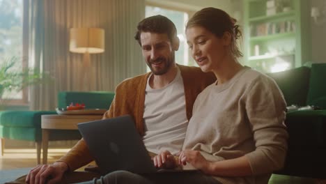 pareja usar computadora portátil, hacer high-five en la celebración, mientras se sienta en la acogedora sala de estar. exitoso novio y novia hablar, comprar en internet, elegir producto para pedir en línea. cámara lenta