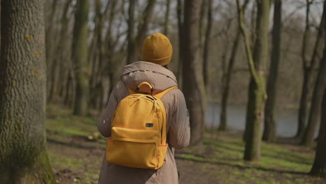 a young girl in a yellow wool cap and a yellow backpack walks through the forest looking from side to side 1