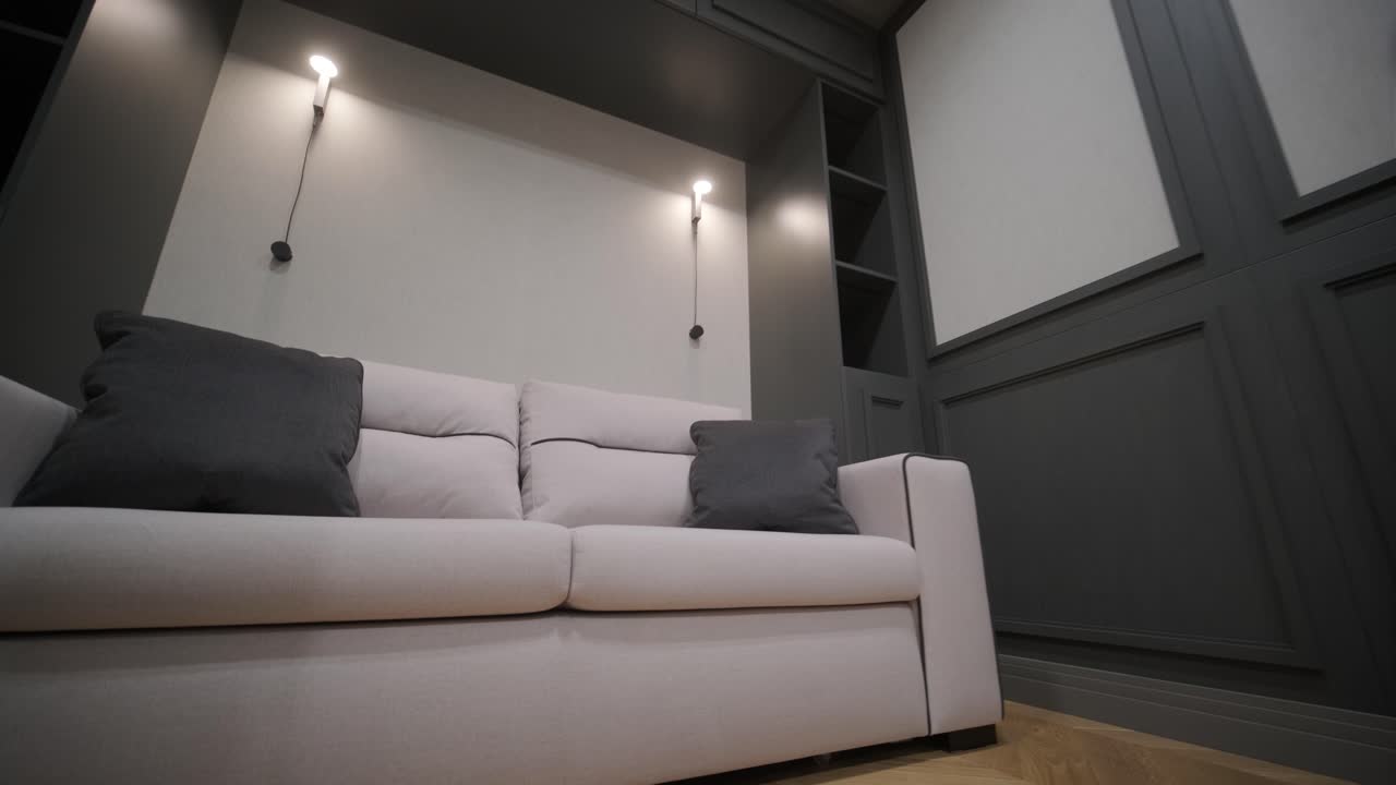 esquina minimalista de la sala de estar con un sofá de tonos neutrales contra una pared de paneles oscuros, complementado por simples luces colgantes y pisos de madera de hueso de arenque