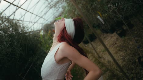 cinematic-medium-shot-video-of-blindfolded-young-woman-leaning-back-while-letting-her-arms-fall-camera-following-her-movements