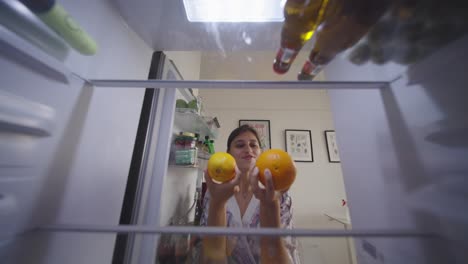 woman holding oranges inside an open refrigerator