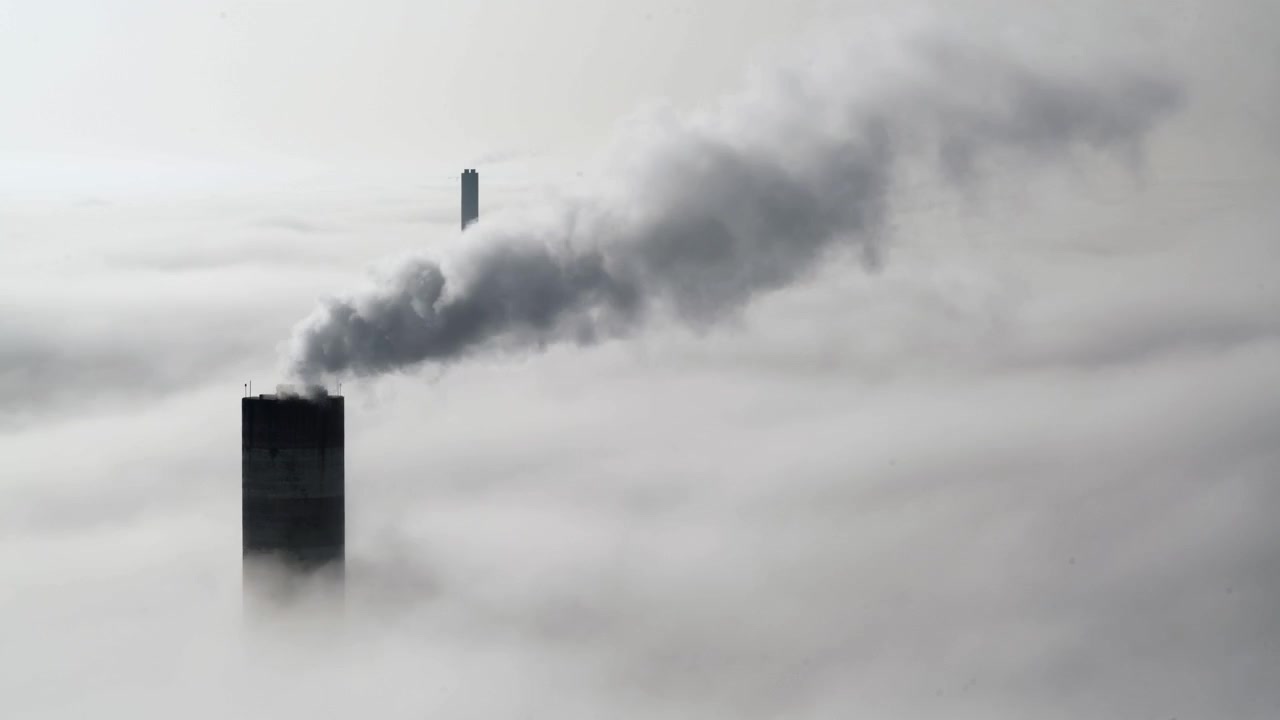 Industrial Chimney Emitting Smoke Above a Thick Layer of Fog