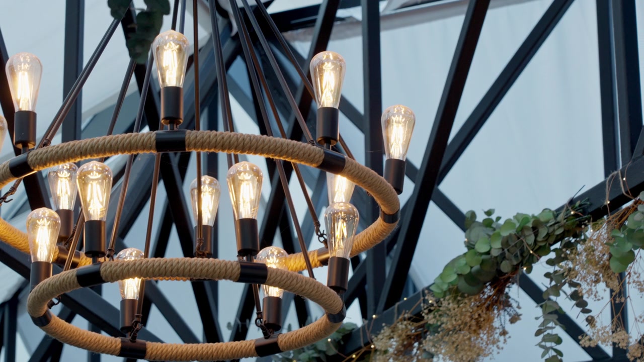 Rustikk industriell lysekrone som lyser opp et moderne arrangementslokale, og skaper en atmosfære med varme, glødende Edison-pærer og dekorativ eukalyptus.