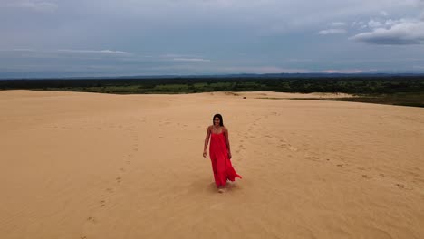 bonita latina con largo cabello oscuro y largo vestido rojo en una enorme duna de arena
