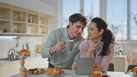 una pareja de tabletas bebiendo café por la mañana juntos en la cocina de cerca.