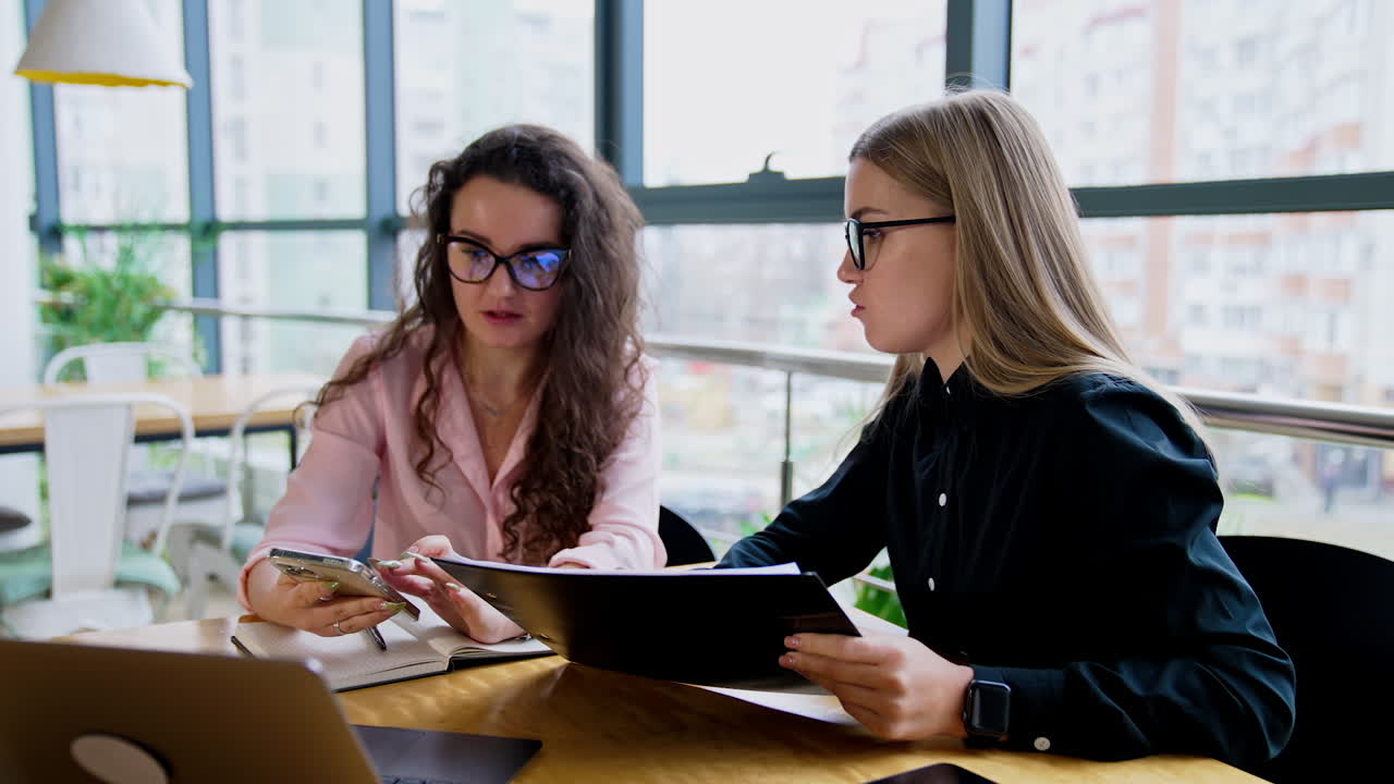 Female coworkers wearing glasses communicate at work. Colleagues using modern technologies for business.