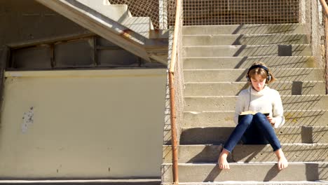 girl listening music while reading a book at beach 4k