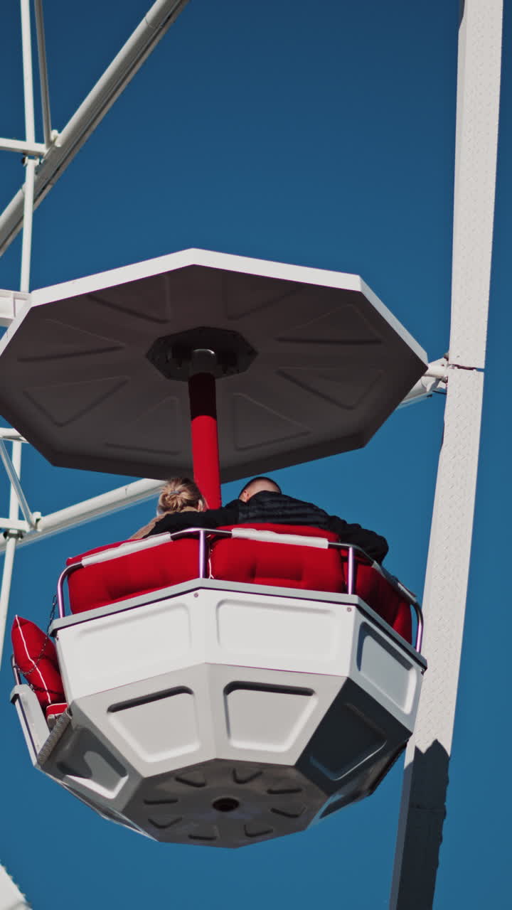 Close up of people in a cabin in a Ferris Wheel with the blue sky on the background. Vertical