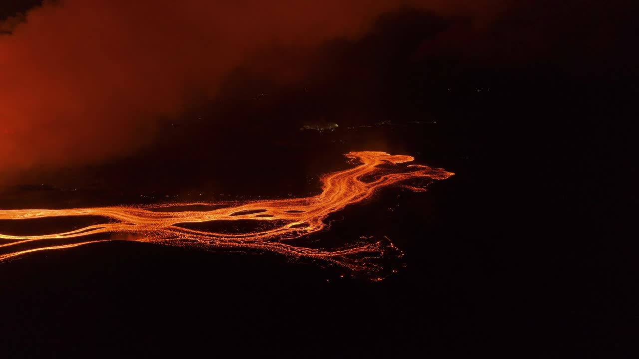 una corriente de lava ramificada que brilla de color naranja en el paisaje nocturno, aérea