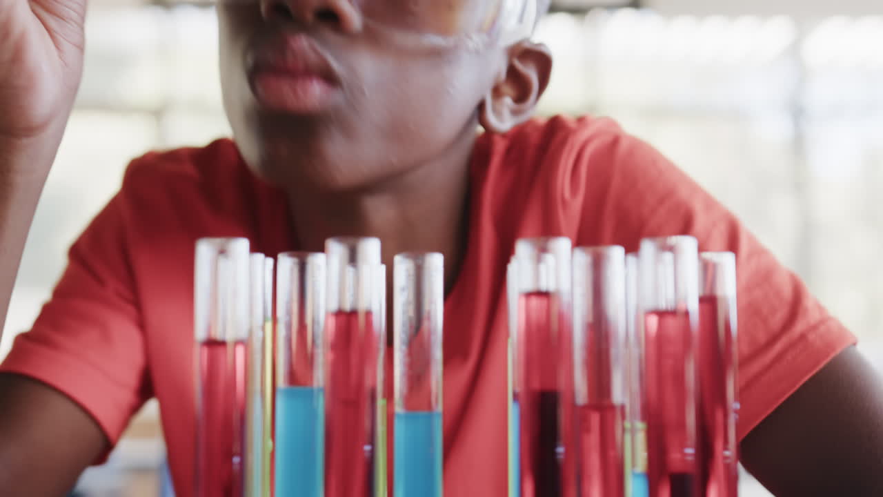 In school, student wearing safety goggles examining test tubes in science class