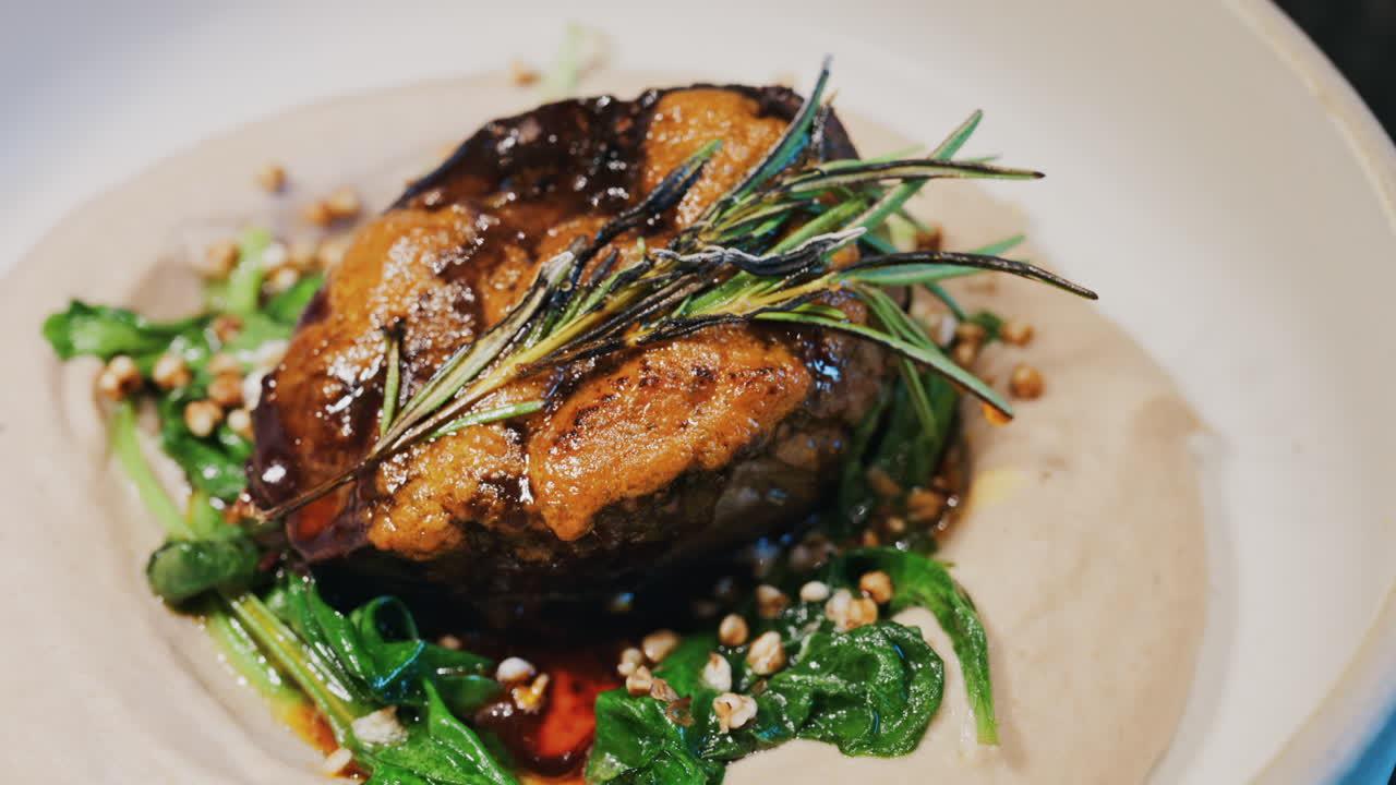 Close up of a beautifully plated beef filet, topped with a golden crust and garnished with rosemary