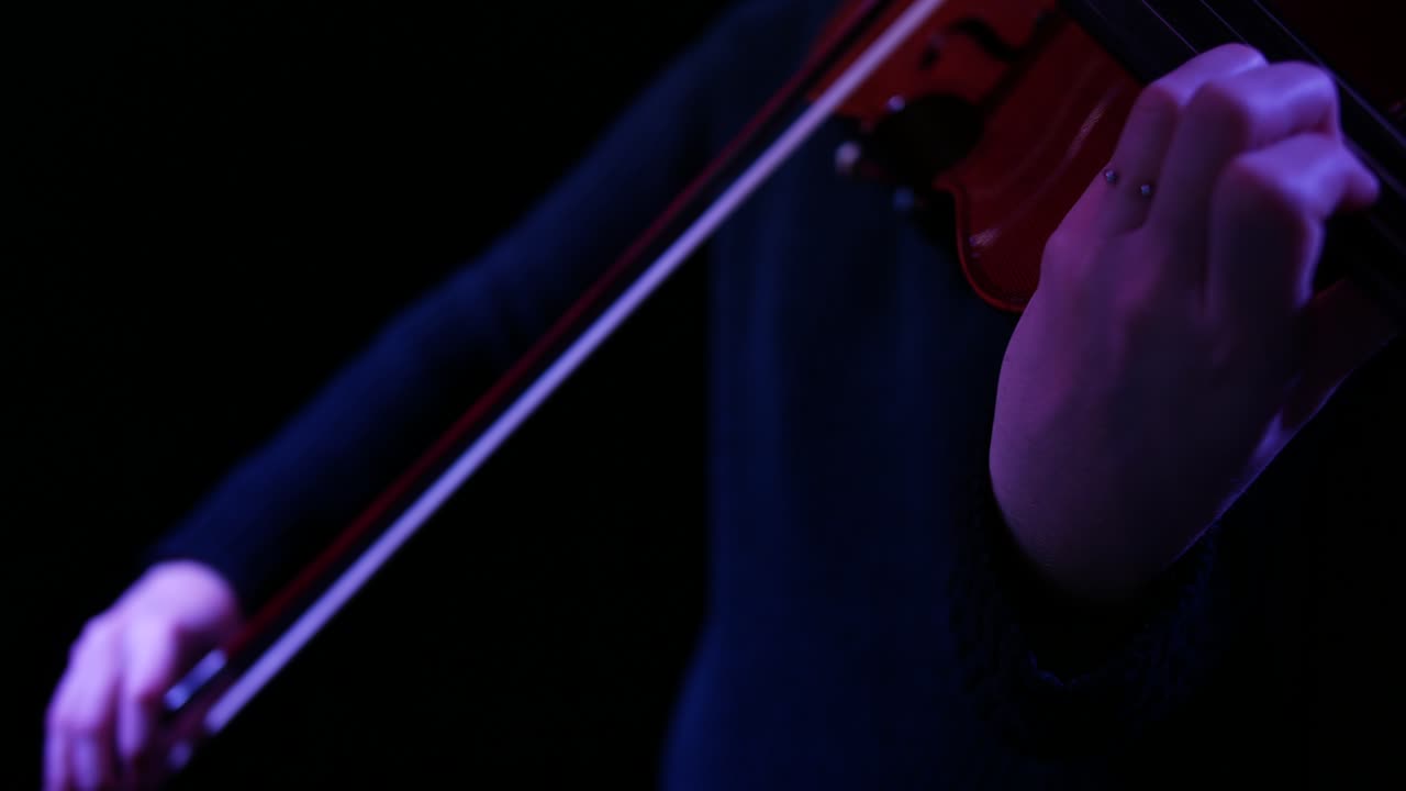 Close-up of Hands Playing Violin with Bow in Dark Setting