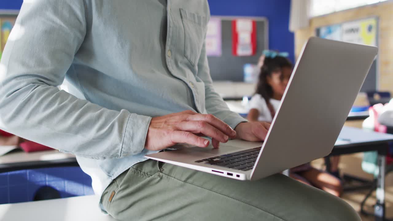 sección media de un maestro caucásico en el aula con niños usando una computadora portátil