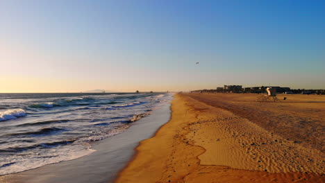 Fly-aerial-4k-drone-from-ocean-waves-at-sunset-onto-empty-beach-and-sand-at-Huntington-Beach,-Southern-California