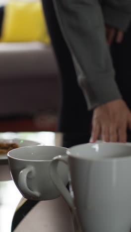 video vertical de primer plano de bebidas calientes en tazas en la mesa en casa con bocadillo con persona en el fondo