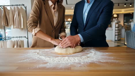 Two professionals in business attire kneading dough together on a floured table