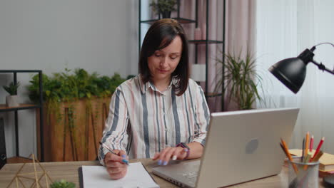 Young-businesswoman-analyzing-documents,-contract-invoices-or-graphics-report-and-working-on-laptop