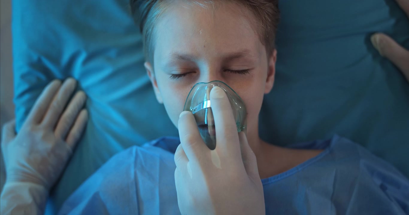 Bambino paziente con maschera per l'ossigeno nel letto d'ospedale