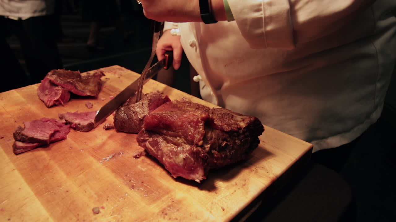 Chef slices meat under heat lamp at event in slow motion